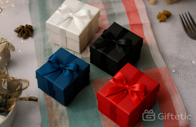 Red, blue, black, and white gift boxes with satin ribbons arranged neatly on a colorful festive tablecloth